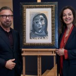 A man, Olivier Widmaier Picasso, and a woman, Péri Cochin, pose for the camera, with a female bust of Picasso displayed on an easel