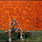 A man sits in front of an orange mural that reads 