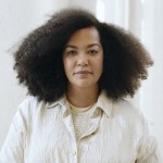 A woman in white looks into the camera from a white background.