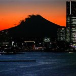 An orange light shone behind the mountains. Skyscrapers stand on one side.