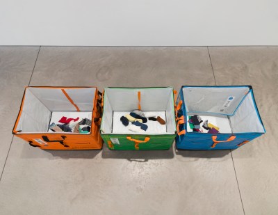 There are three bins on the floor of the gallery, each with a few socks at the bottom.