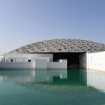 Exterior of a white building with gray lattice dome roof on a green-blue lake.
