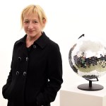 A woman stands next to a globe covered in reflective tiles.
