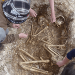 A man looks into a hole containing human remains.