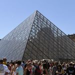 Outside, a group of people stood next to a large glass pyramid structure against a blue sky.