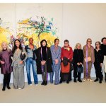 A group of people line up for a photo in front of an abstract painting.