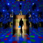 A man walks through a dark room filled with blue lights, polka dots, and mirrors.