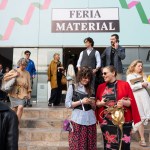 A group of trade show attendees exit a building. There is a sign above the head that says "Feria material."
