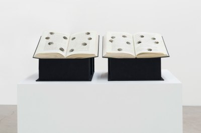 A sculpture composed of two open history books, each with huge bullet holes.