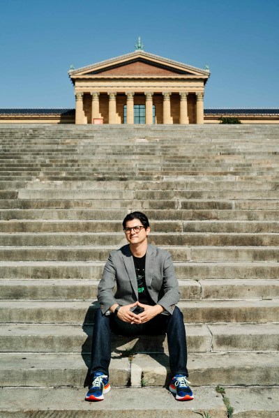 A white man, curator Paul Farber, sat on the steps outside the Philadelphia Museum of Art. The classical Greek-style exterior of the museum can be seen at the top of a flight of stone steps.