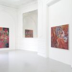 Abstract paintings hang on the white walls of the gallery.