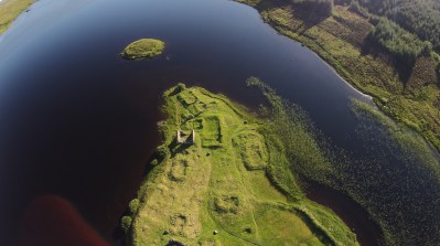 An aerial view of a green isle in the middle of a loch.