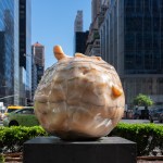 A sculpture of water droplets in front of a bush.