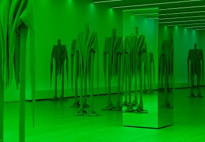 Devices in the room light up green. Tall figures covered in fabric gather around mirrored columns.