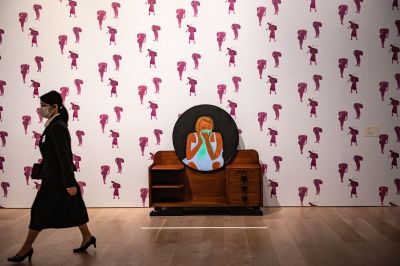 A woman walks past a dressing table where a circular painting of a crying woman hangs.