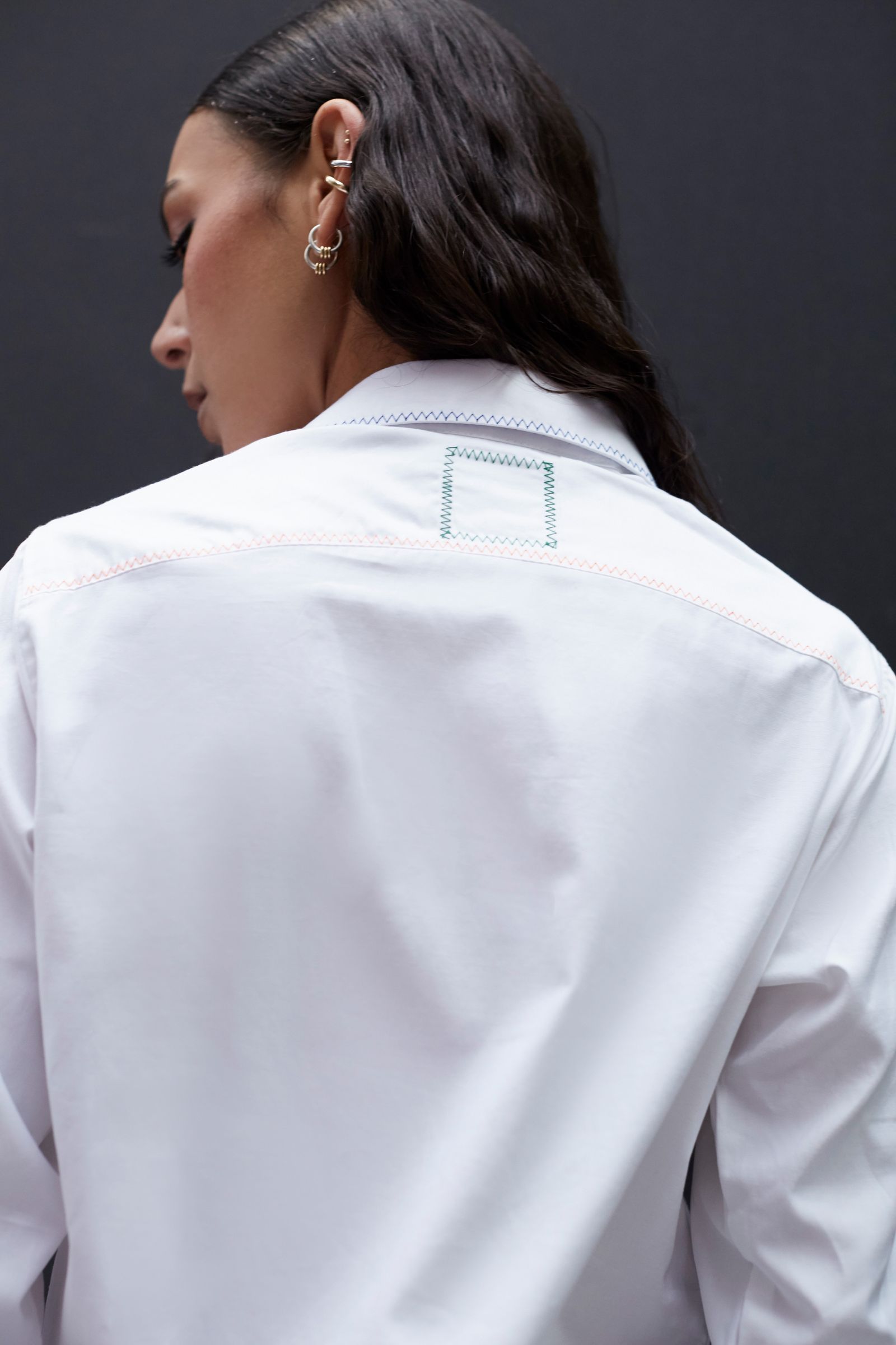 Image may contain clothing, coats, lab coats, shirts, adult accessories, earrings, jewelry, shirts, face and head