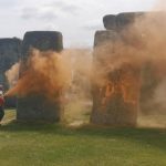 Two protesters spray orange powder paint on the Stonehenge monument.