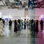 A performance artist (left) walks through the aisles of the third edition of ART SG, his reflection reflected in an artwork made of brightly colored acrylic.