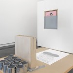 Hanging from the ceiling is a portrait with a pink background, two-thirds of which is covered in gray paint, obscuring the subject.