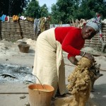 A portrait of Seyni Awa Camara leans against a sculpture, smiling, with a bucket of wet clay beside her.