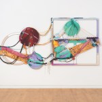 A colorful abstract piece composed of multiple painted circles and rectangles, crisscrossed by ropes, hangs on the wall.