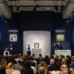 Auctioneer gestures in front of a crowded auction room.