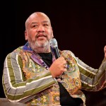 A man in a colorful jacket holding a microphone.