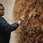 Delcy Morelos, wearing a blue jumpsuit, places hay into a large sculpture made of earth.