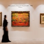 A woman stands in front of three paintings.