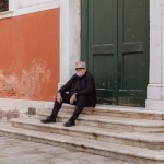 A man dressed in black sat on the steps next to a large door.