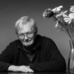 A man sits on a table with his arms crossed and a bouquet of flowers next to him.