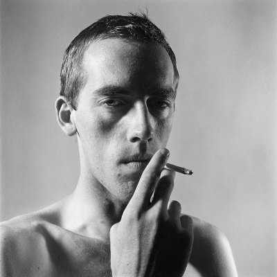 Over the shoulder, a shirtless man smokes a cigarette. 