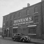 From one angle, a three-story brick house. On the front it says: "Bonhams Old Chelsea Auction Gallery" Use capital letters. An old car parked in front of it.