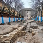 Archaeological excavations between two yellow buildings showing ruins from ancient Roman times.