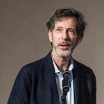 A man in a suit speaks into a microphone.