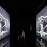 A woman is looking at a screen depicting a painting by a man.