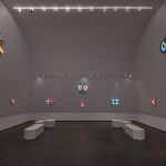 A dark gallery with light sculptures hanging on the walls.