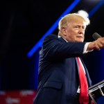 Donald Trump, wearing a suit and red tie, stood in front of a microphone and pointed into the distance.