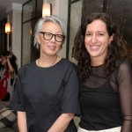 Two women stood side by side, both wearing black tops from the waist up. One has chin-length gray hair and wears glasses, the other has brown curly hair that falls past his shoulders.