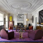 A very nice living room with purple chairs, purple rug and lots of art.