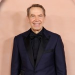 A man in a suit stands under a set of pink arches.