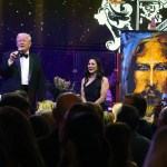 A man in a tuxedo stands next to a woman, and a bearded man is depicted in the painting.