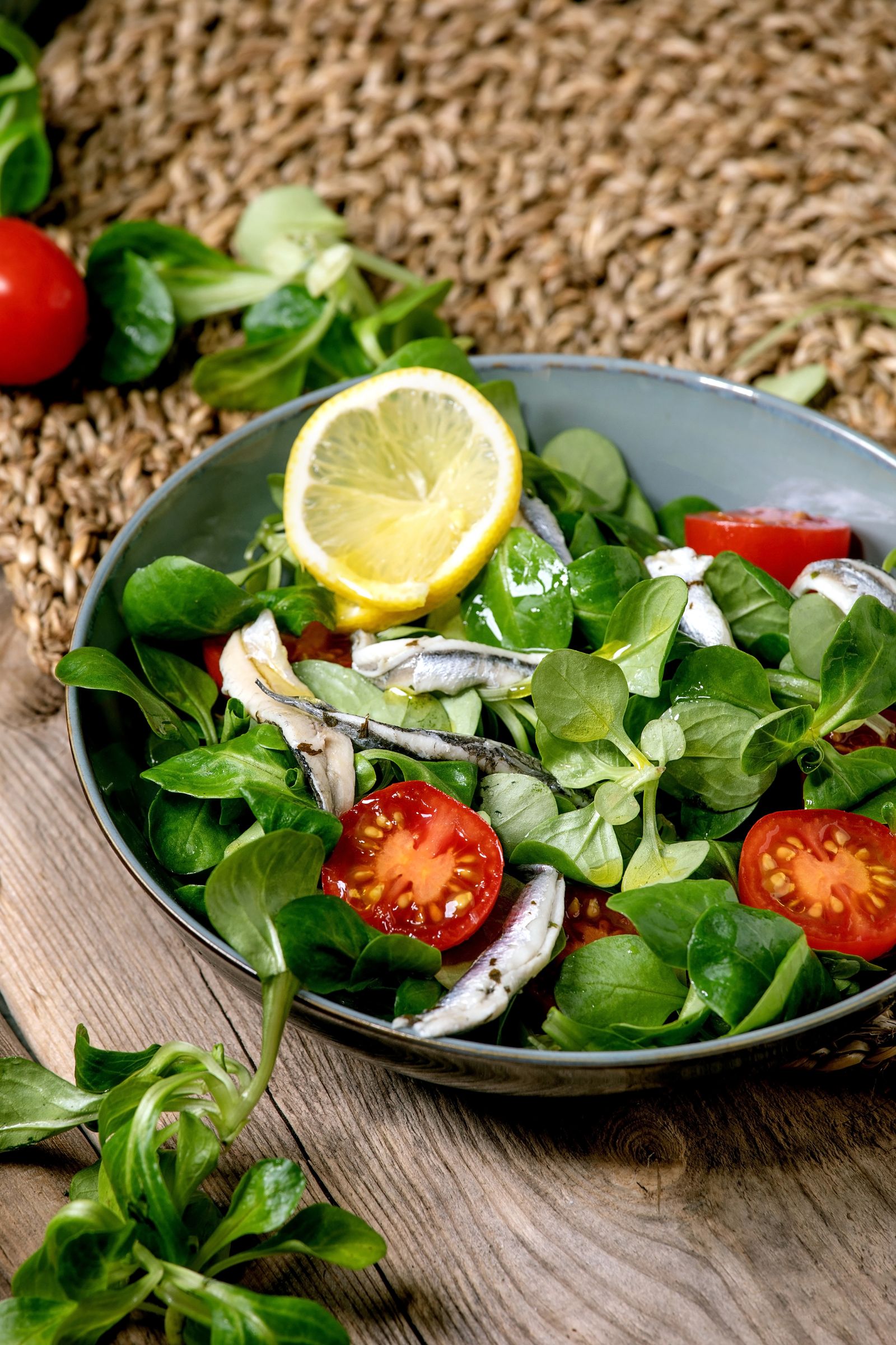 Green field salad with pickled anchovies or sardine fillets and cherry tomatoes in a blue bowl with lemon and olives...