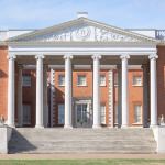 Exterior view of a red brick building with gables and Ionic columns on the facade.