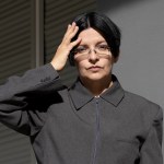 Portrait of Henrik Naumann, wearing gray jacket with zipper and collar, holding one hand on his head.