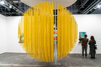 A yellow plastic sculpture hangs in the center of an art fair booth.