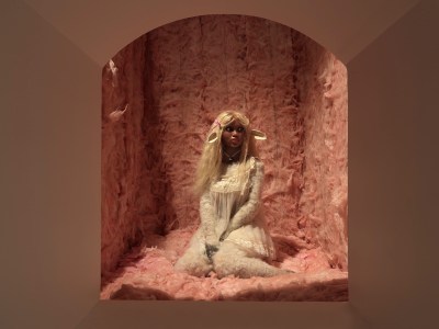 A black animatronic figure kneels in a recess lined with pink tufted material.