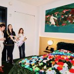 Three people look at soft sculptures displayed on a hotel bed.