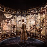 A woman stands in front of a large artwork that resembles a painted screen.