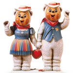Sculptures of a male and female bear wearing matching clothes, smiling, rosy cheeks and waving.